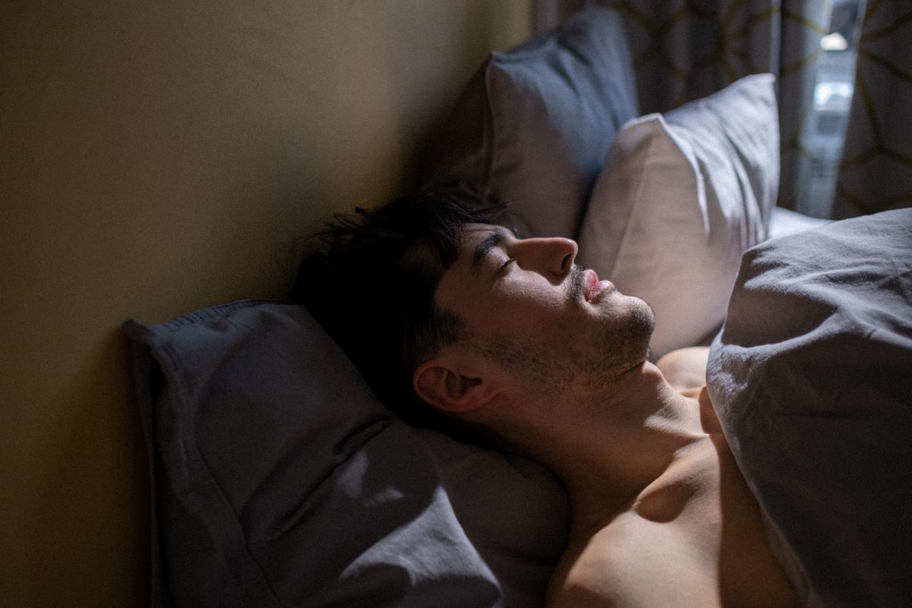 A man lying in bed asleep, head tilted back against a pillow.