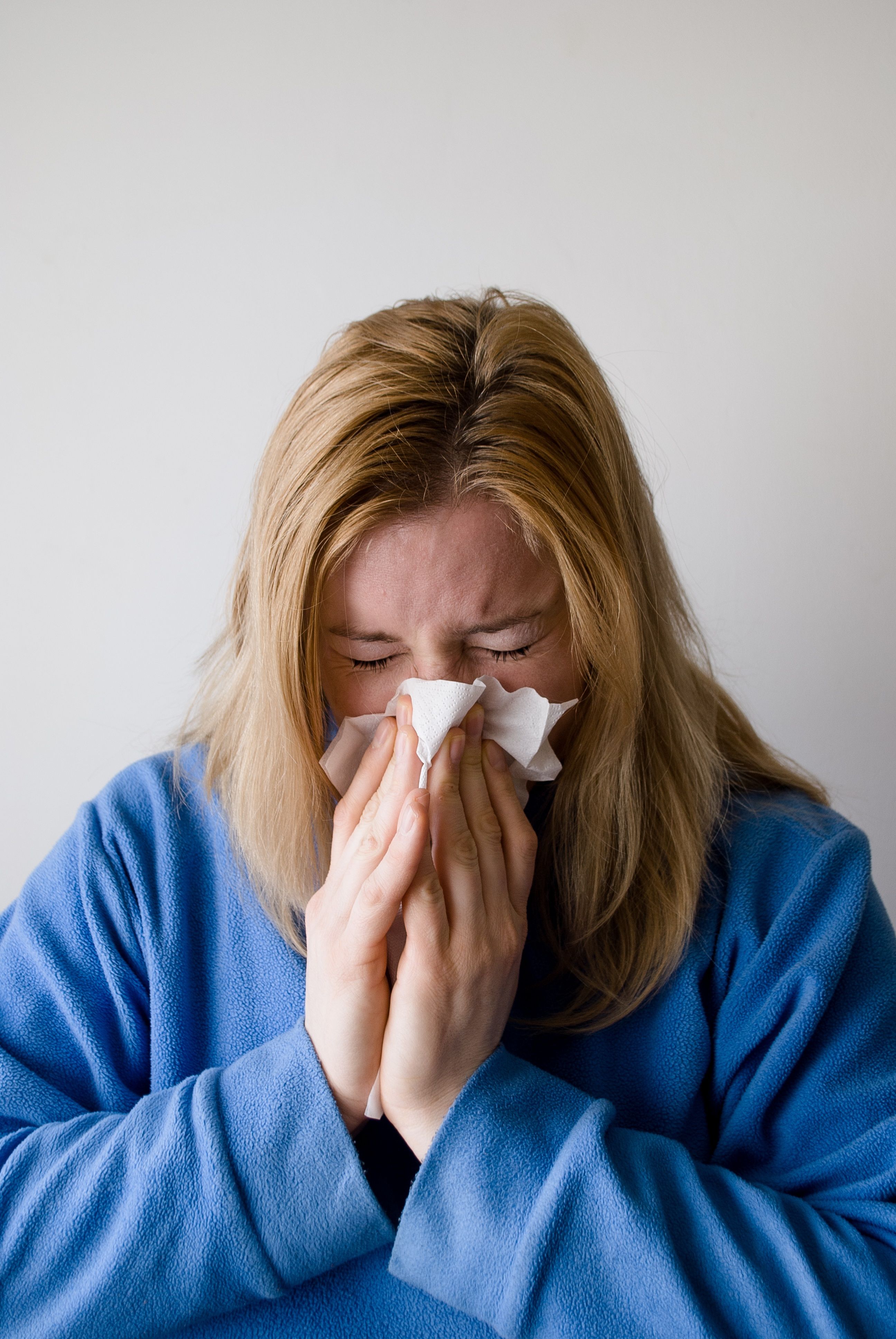 A woman with a runny nose blows her nose into a tissue, appearing to have a cold or allergies.