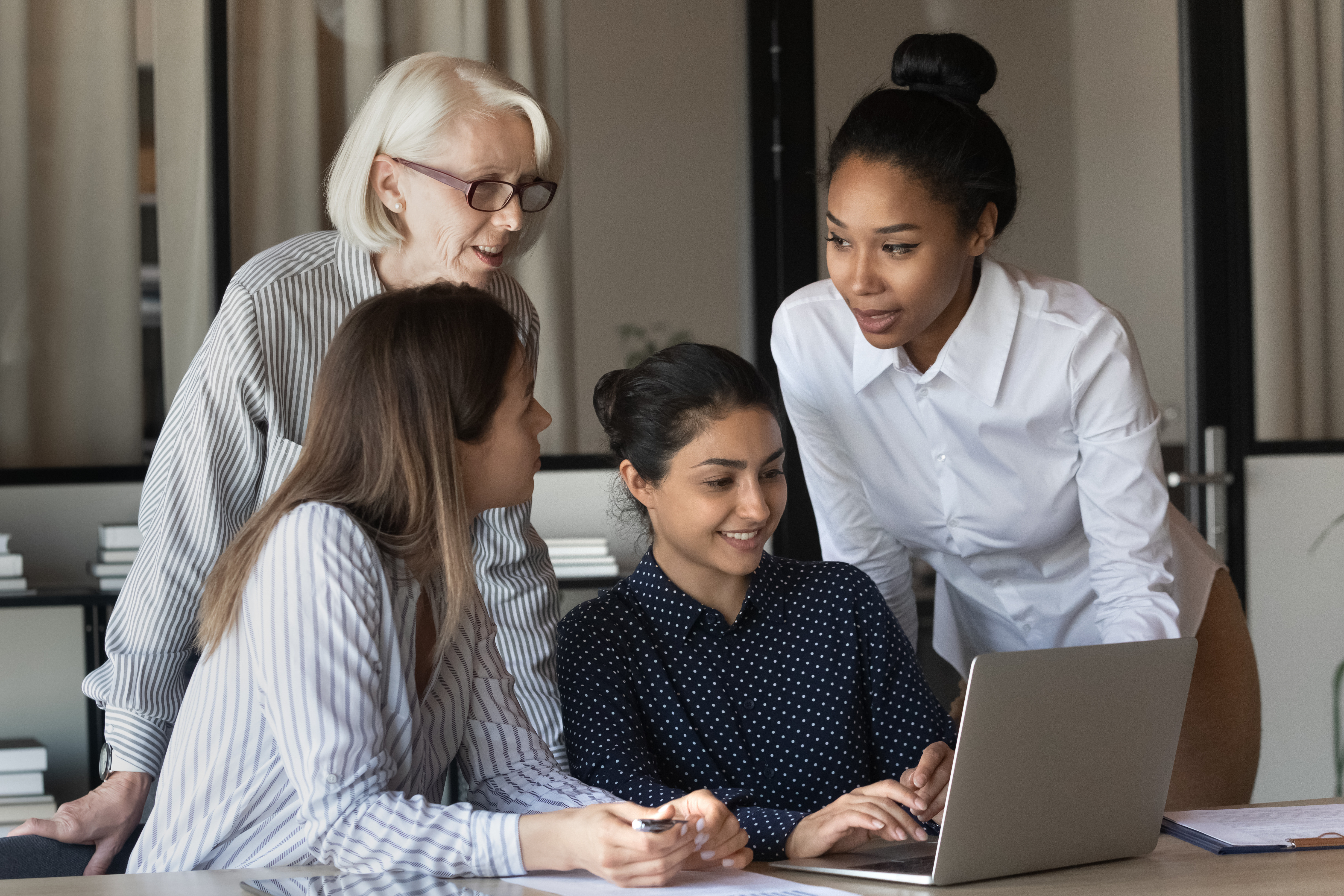 Four women collaborating around a laptop in an office, marked as a featured article