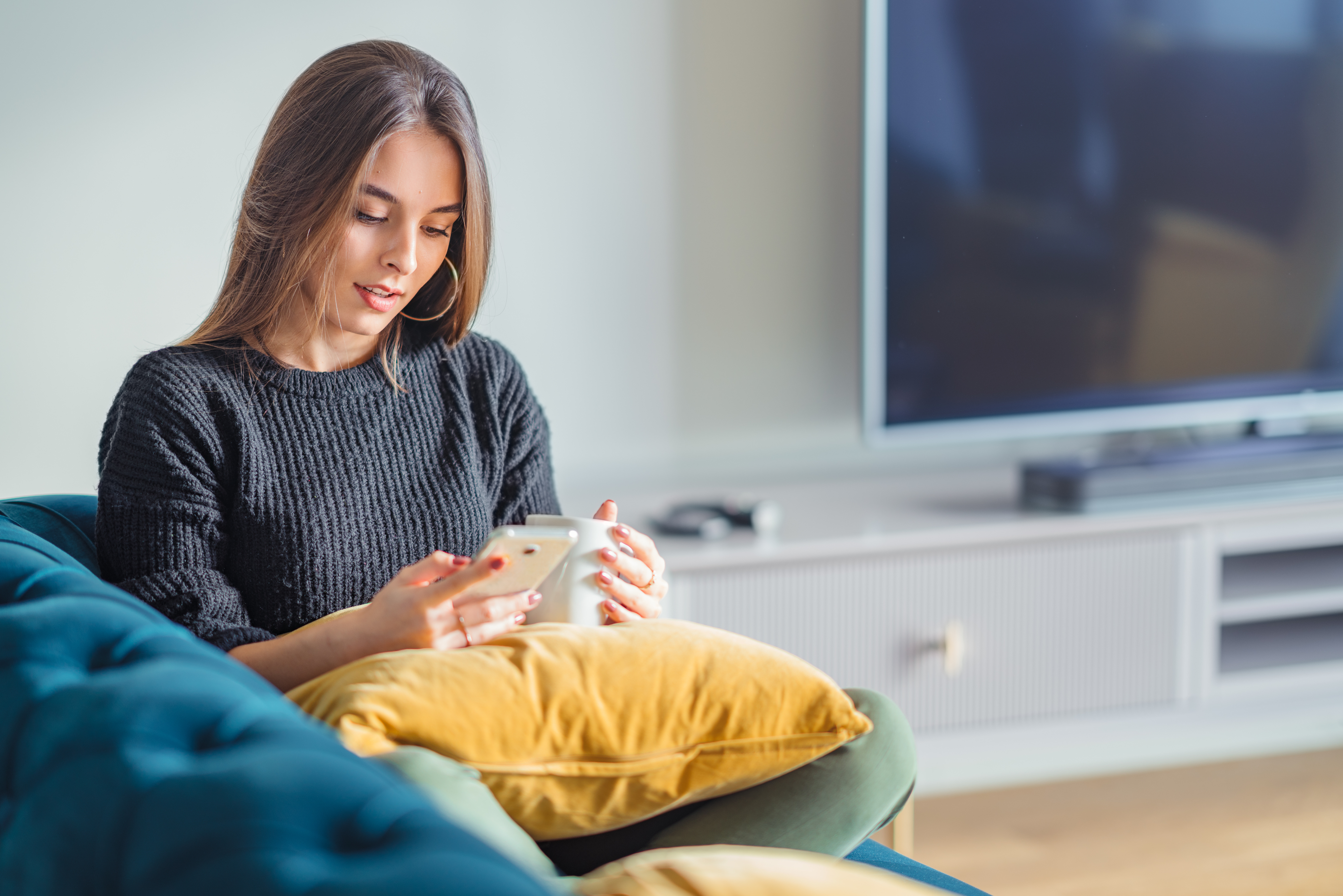 Woman relaxing on a sofa with yellow cushions, looking at her phone, marked as a featured article