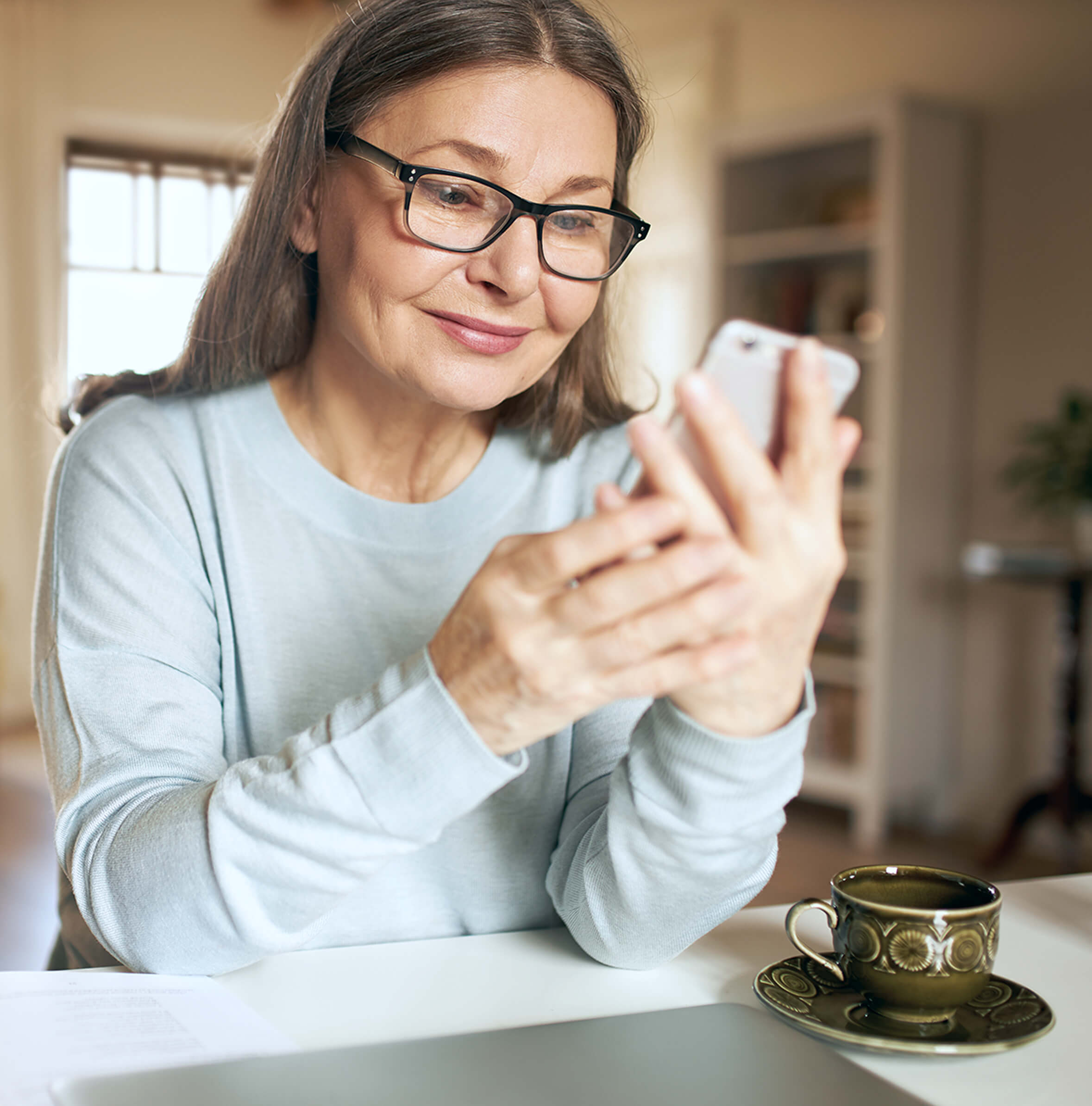 Women looking at a phone while sitting down at a table with a cup and saucer on table