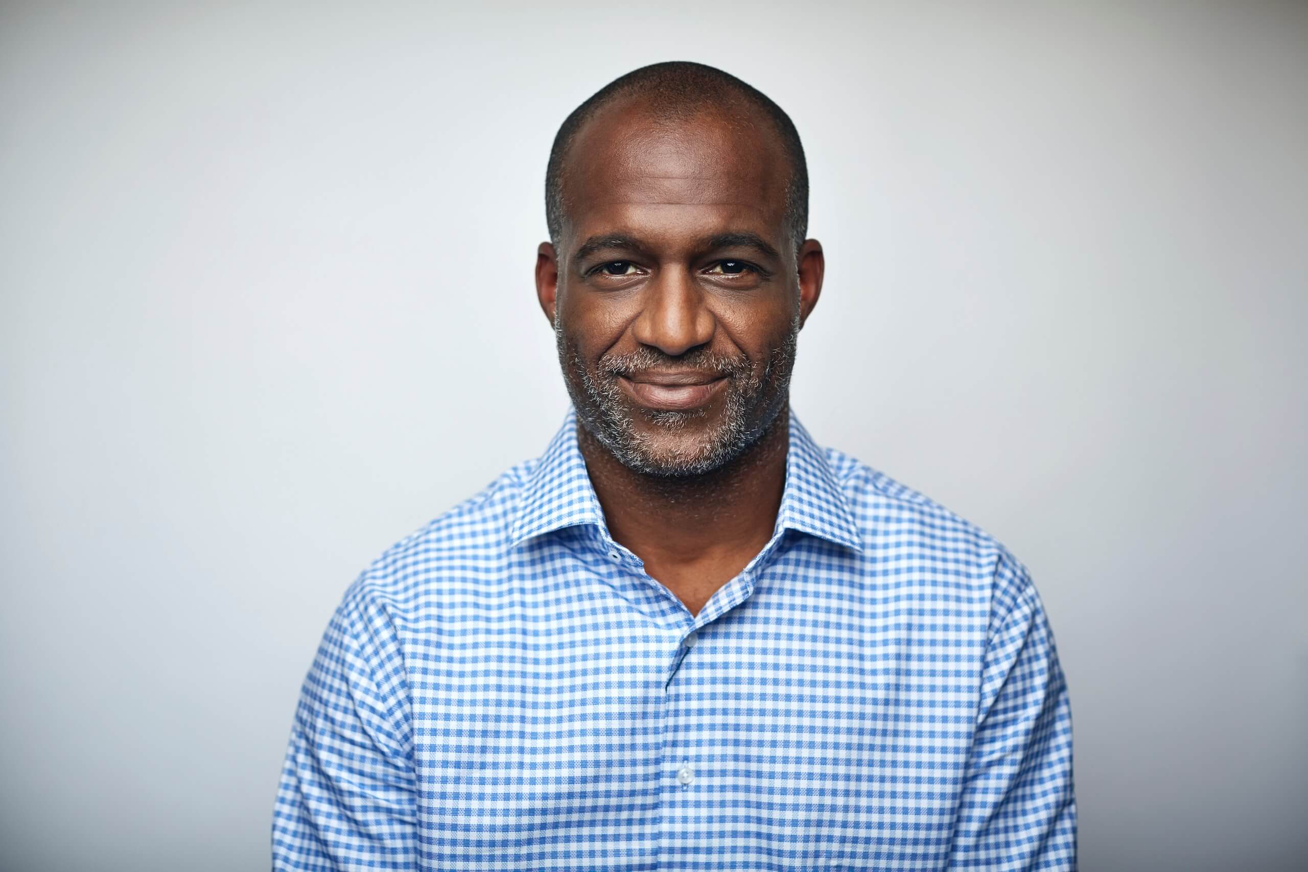 Smiling man in a blue checked shirt posing for a portrait against a grey background