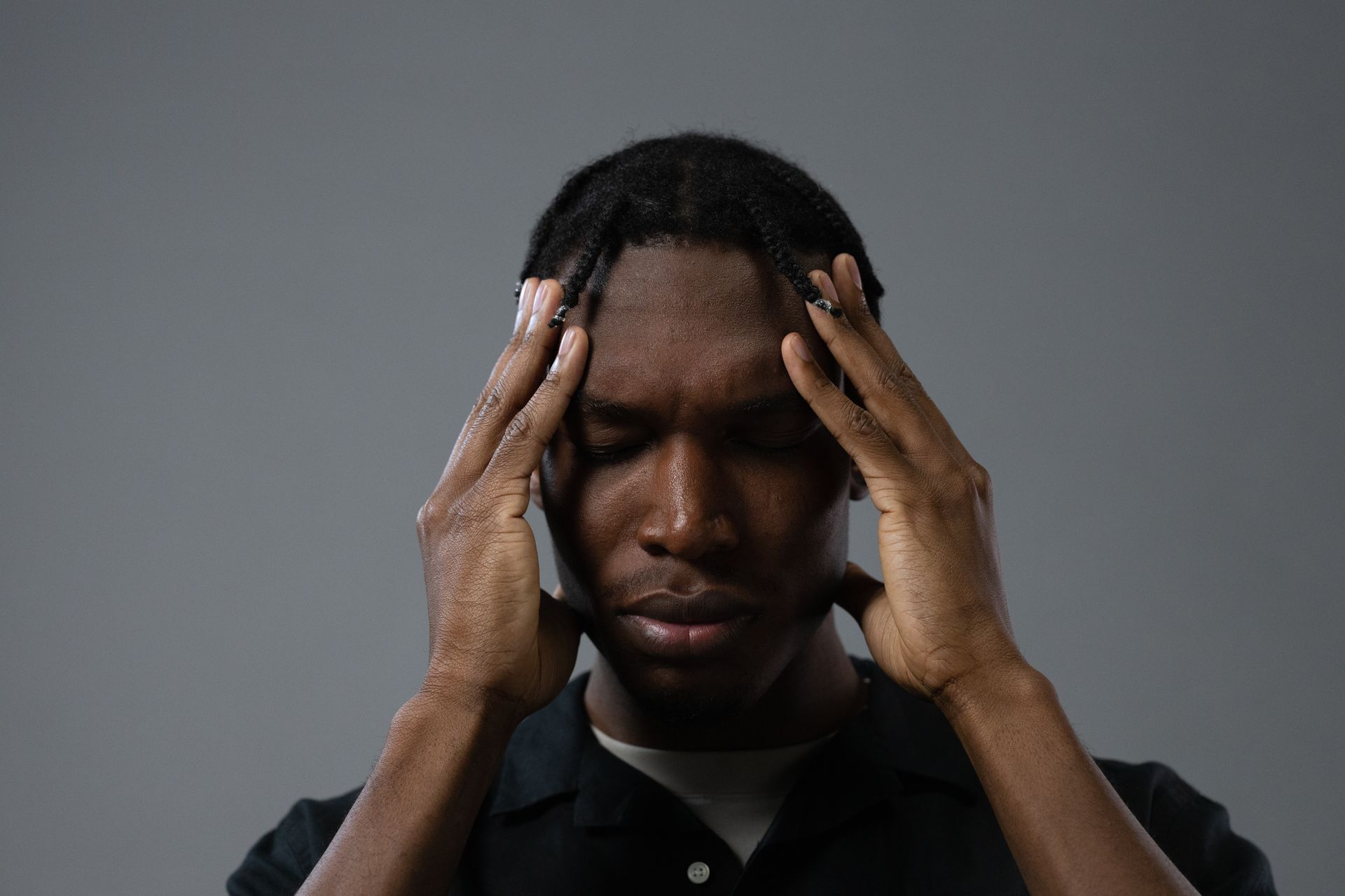 A man pressing his fingertips to his temples, appearing to experience a headache, against a plain grey background.