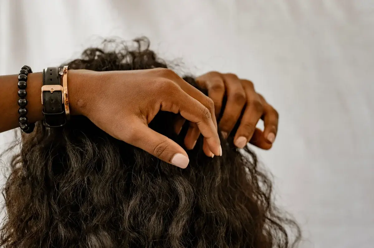 Close-up of a person’s hands scratching their scalp through dark, curly hair